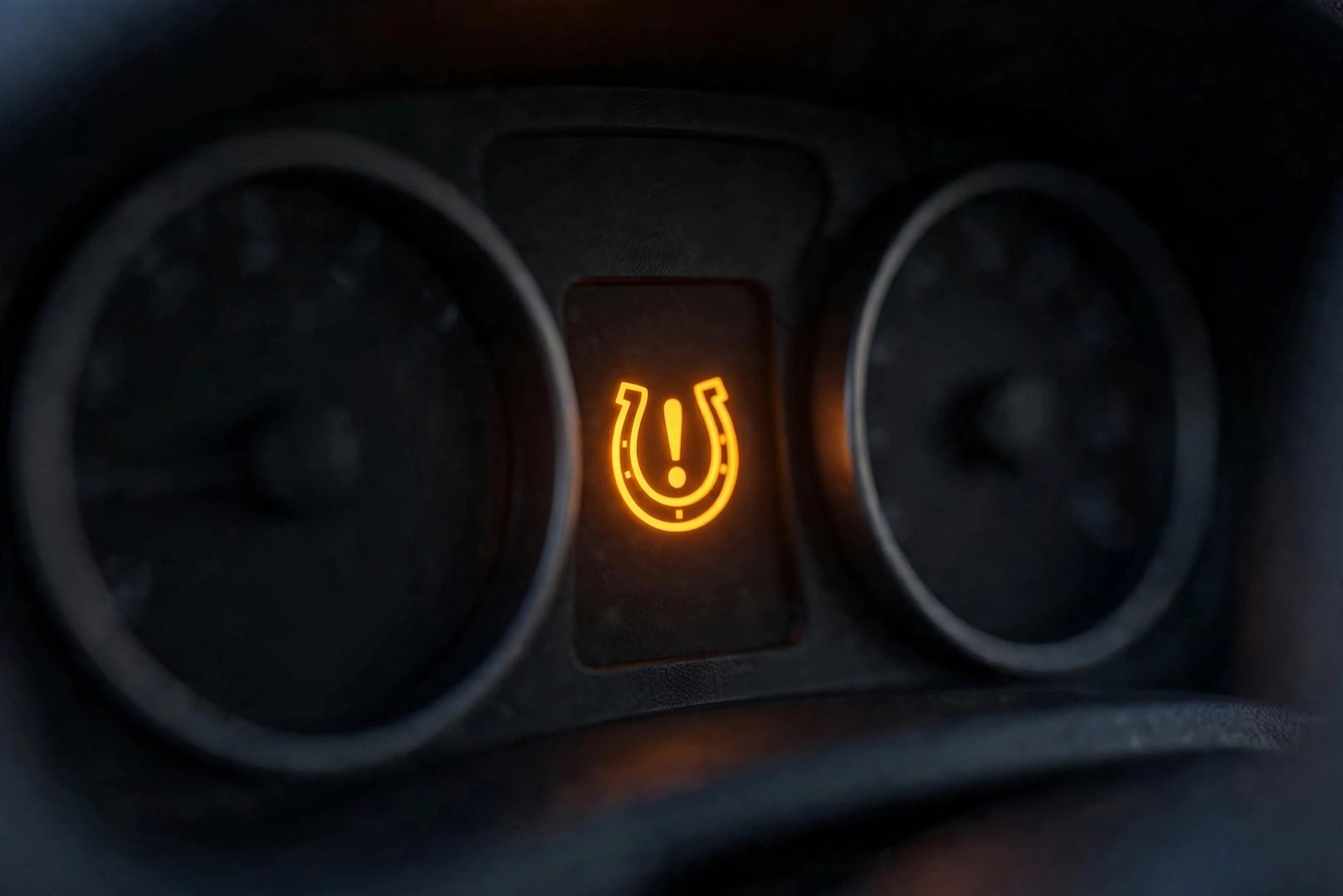 Yellow tire pressure TPMS warning light glowing on a car dashboard at night